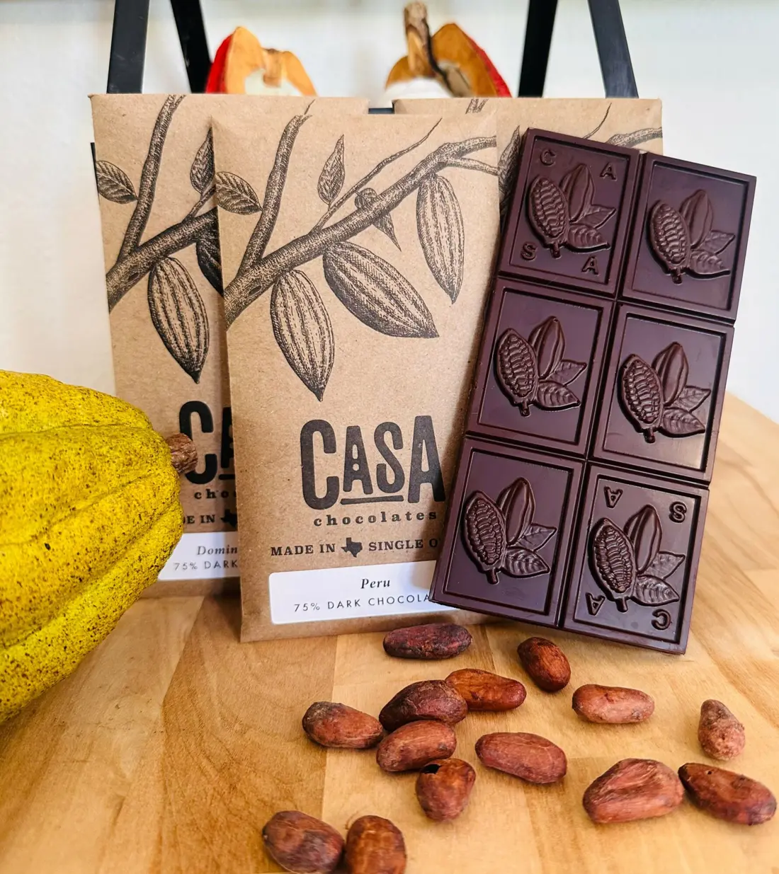 A Casa Peru 75% dark chocolate bar lying on its kraft wrapper, with cacao beans and a cacao pod
